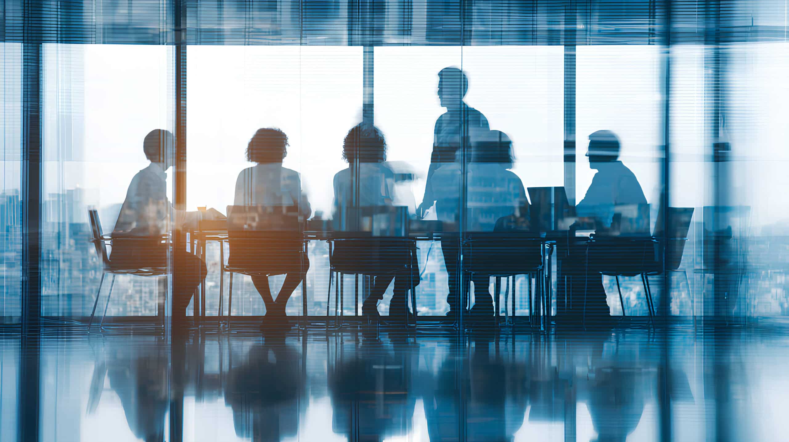 Business professionals meeting in a glass-walled conference room, with one person presenting to the group.